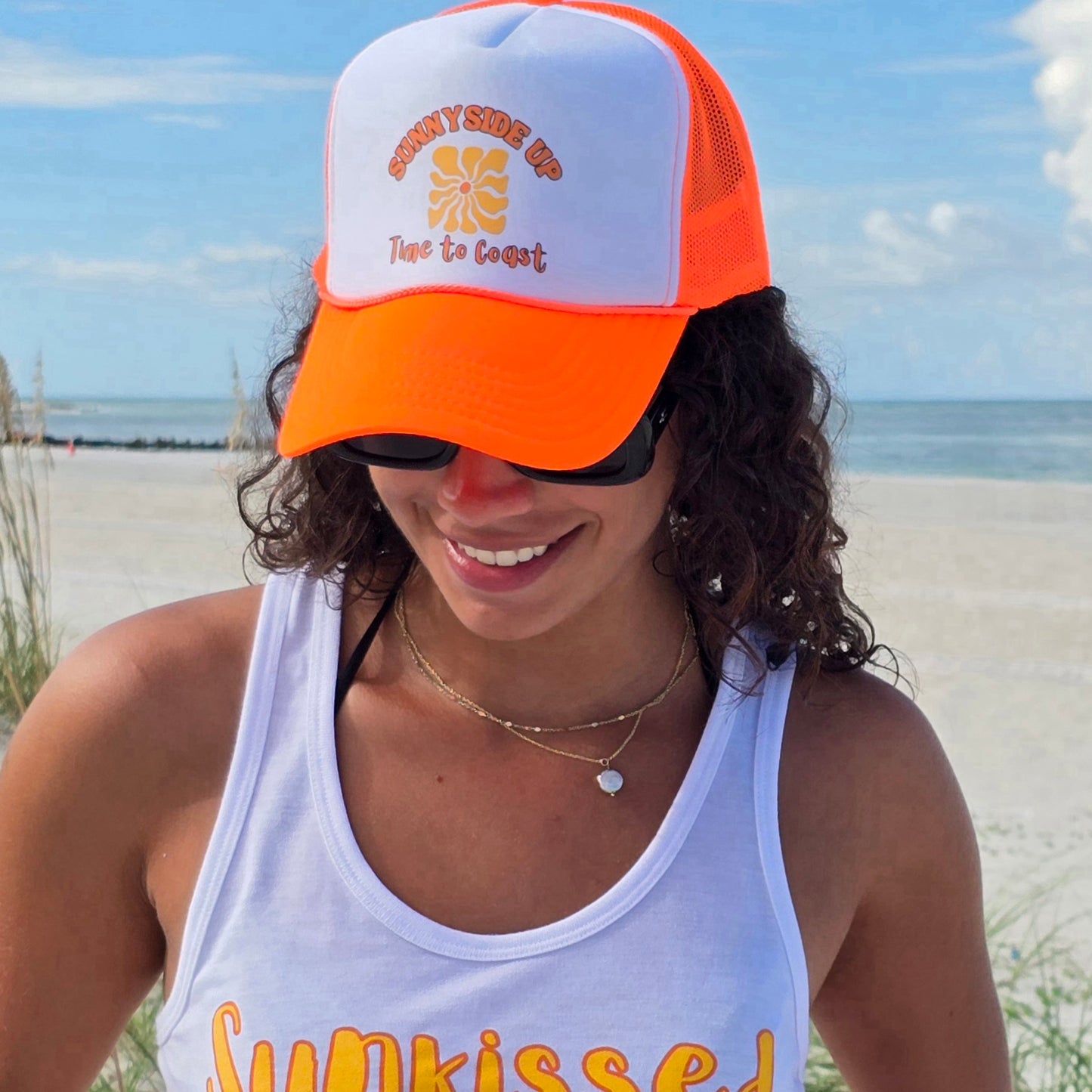 Woman wearing a foam high profile trucker hat. Graphic is printed with Time to Coast Sunnyside Up Sun. Hat color is bright orange bill and mesh back with white front.