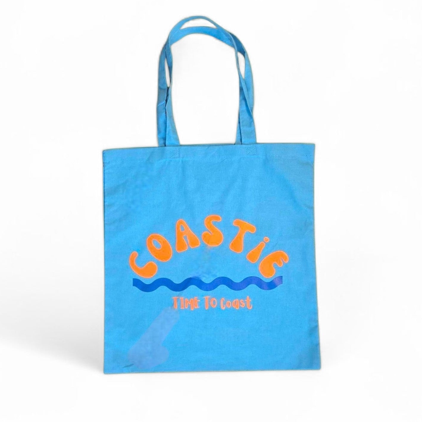 laydown of a turquoise Market Bag. Bag has a Coastie word graphic, wave and time to coast logo