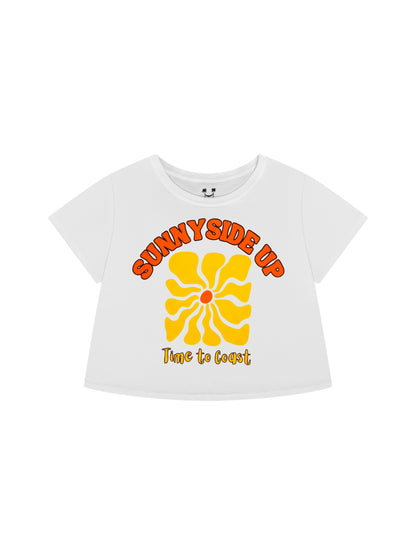 Laydown of a white Time to Coast Palm Cloth crop tee. Graphic is Sunnyside Up Sun, in yellow and orange colors.  