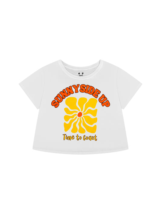 Laydown of a white Time to Coast Palm Cloth crop tee. Graphic is Sunnyside Up Sun, in yellow and orange colors.  