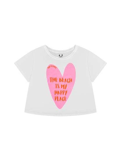 Laydown of a white Time to Coast Palm Cloth crop tee. Graphic is a heart with beach is my happy place slogan. Heart color is pink with red wording. 