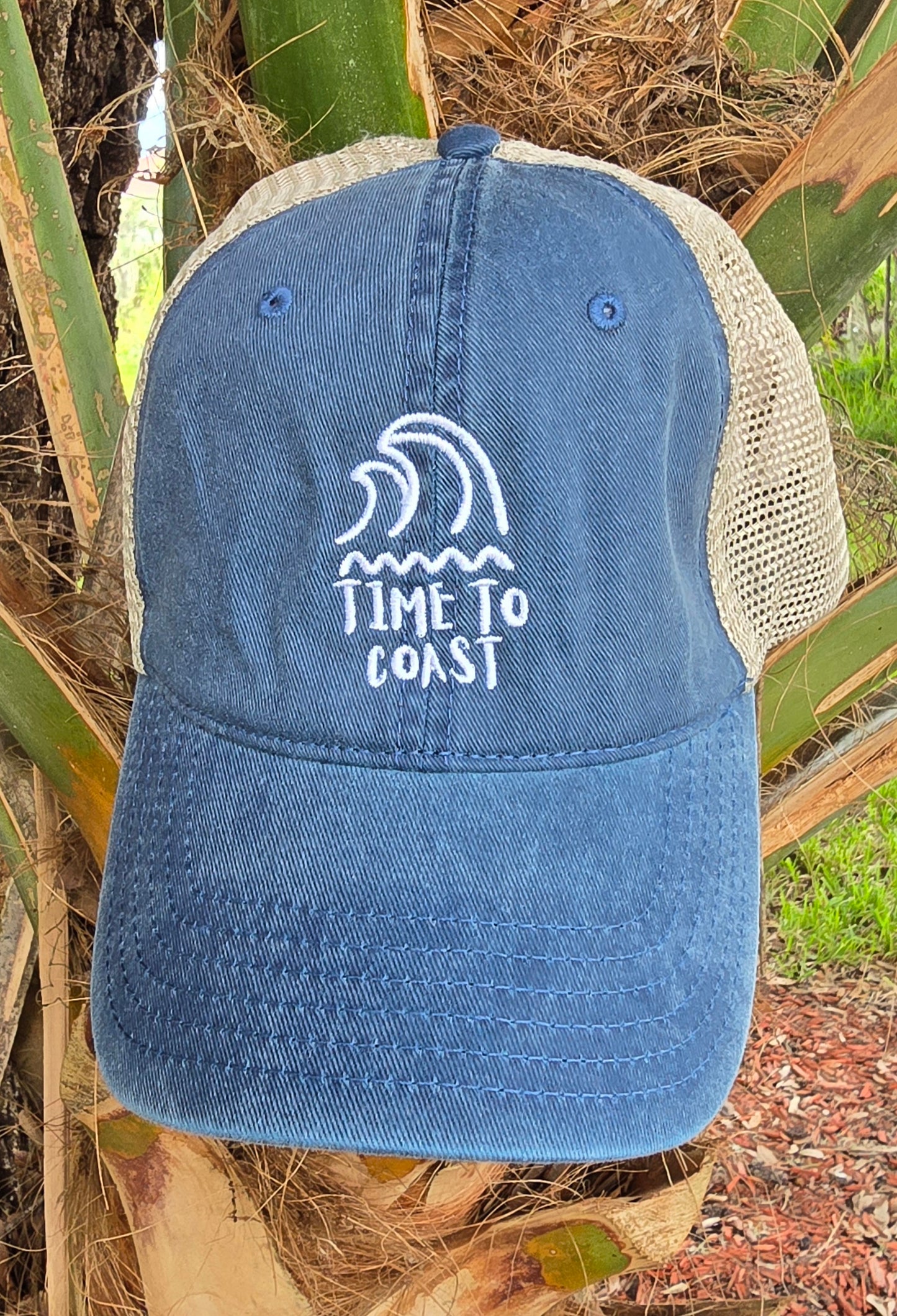 Laydown of the Time to swell low profile trucker washed navy twill hat with tan mesh back. Graphic is an embroidery of surf swell and waves with time to coast in white.