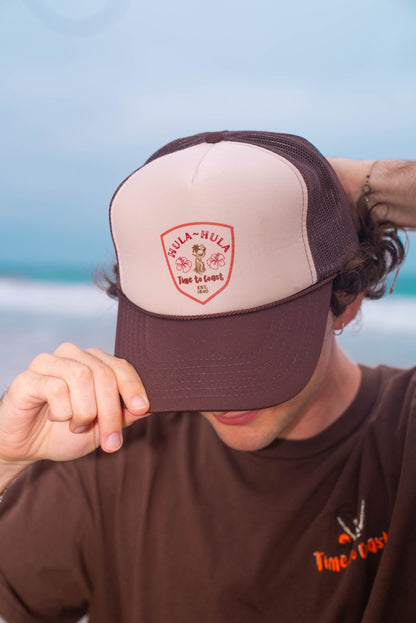 Man wearing a foam high profile trucker hat.  Graphic is printed with Time to Coast Hula Hula girl. Hat color is beige and brown with a brown mesh back.