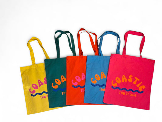 laydown showing 5 colors of the Market Bag. Yellow, green, orange, turquoise and hot pink.  Bag has a Coastie word graphic, wave and time to coast logo