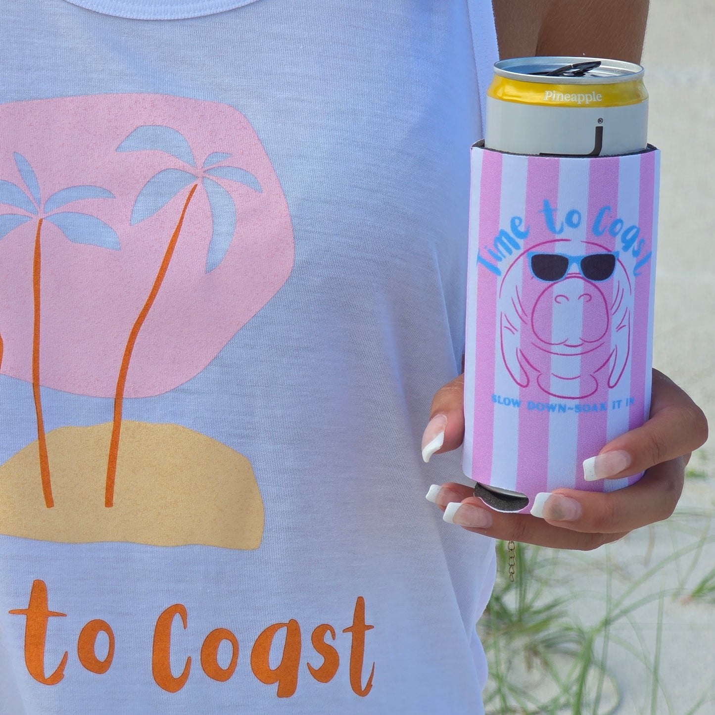 close up of the coozie, woman wearing a time to coast ,my island palm cloth tank, holding a neoprene slim coozie with a graphic of a manatee wearing sunglasses