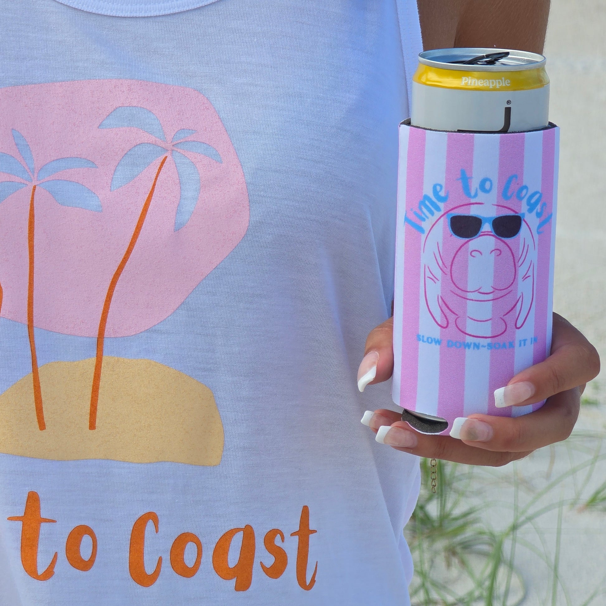 close up of the coozie, woman wearing a time to coast ,my island palm cloth tank, holding a neoprene slim coozie with a graphic of a manatee wearing sunglasses