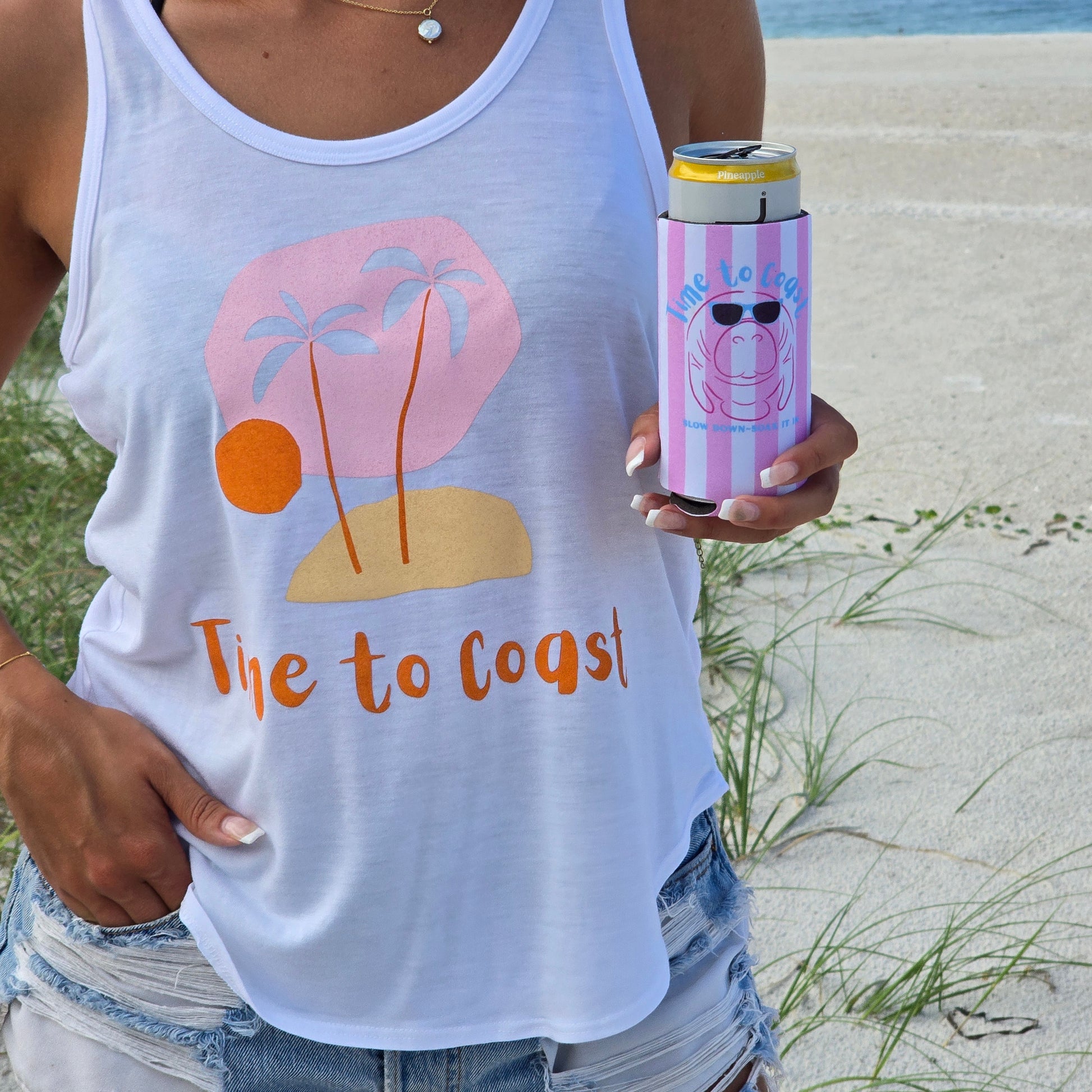 woman wearing a time to coast ,my island palm cloth tank, holding a neoprene slim coozie with a graphic of a manatee wearing sunglasses