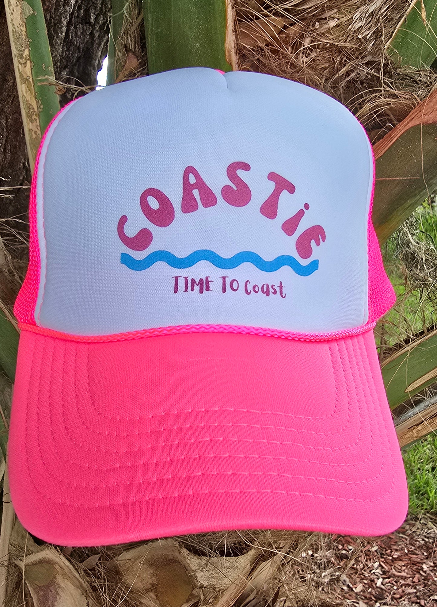 Laydown of a foam high profile trucker hat.  Graphic is printed with Time to Coast Coastie with waves. Hat color is bright pink bill and mesh back with white front. 