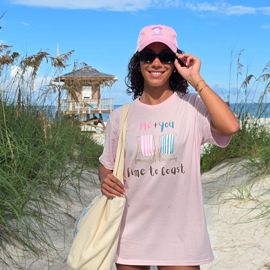 woman in the dunes of a beach wearing a light pink color graphic  t-shirt in organic cotton made in USA and a pink hat, glasses and hobo fleece beach bag. Homegrown t-shirt with a large front graphic of 2 beach chairs with Me + You.  Model is wearing a boyfriend fit size.