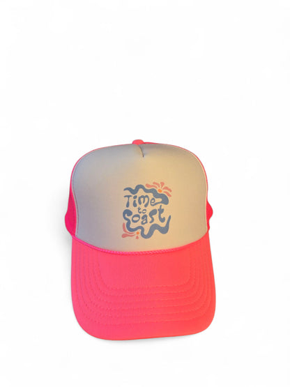 Laydown of a foam high profile trucker hat.  Graphic is printed with Time to Coast Hippy Wave. Hat color is bright pink bill and mesh back with white front. 