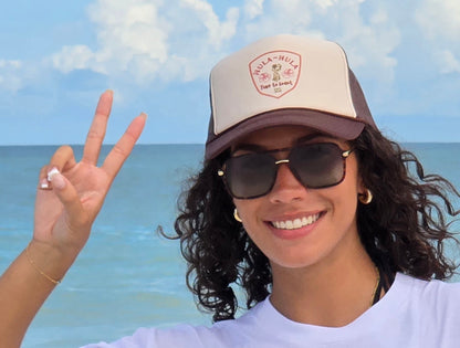 Woman wearing sunglasses at the beach and a foam high profile trucker hat.  Graphic is printed with Time to Coast Hula Hula girl. Hat color is beige and brown with a brown mesh back.