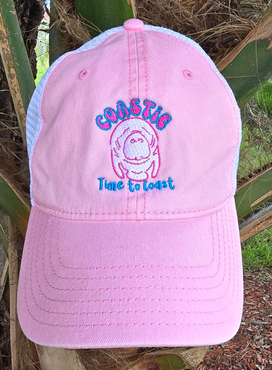 Laydown of the Coastie Manatee embroidered twill low profile trucker hat. Color of hat is washed pink twill with a white embroidered manatee and tan mesh back.