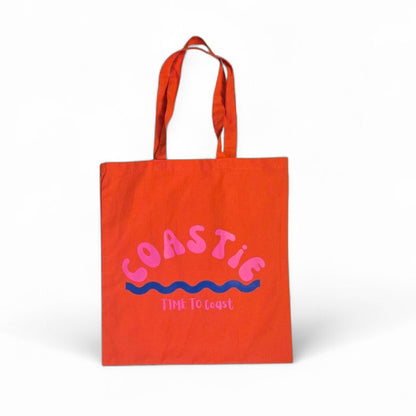 laydown of a orange Market Bag.  Bag has a Coastie word graphic, wave and time to coast logo